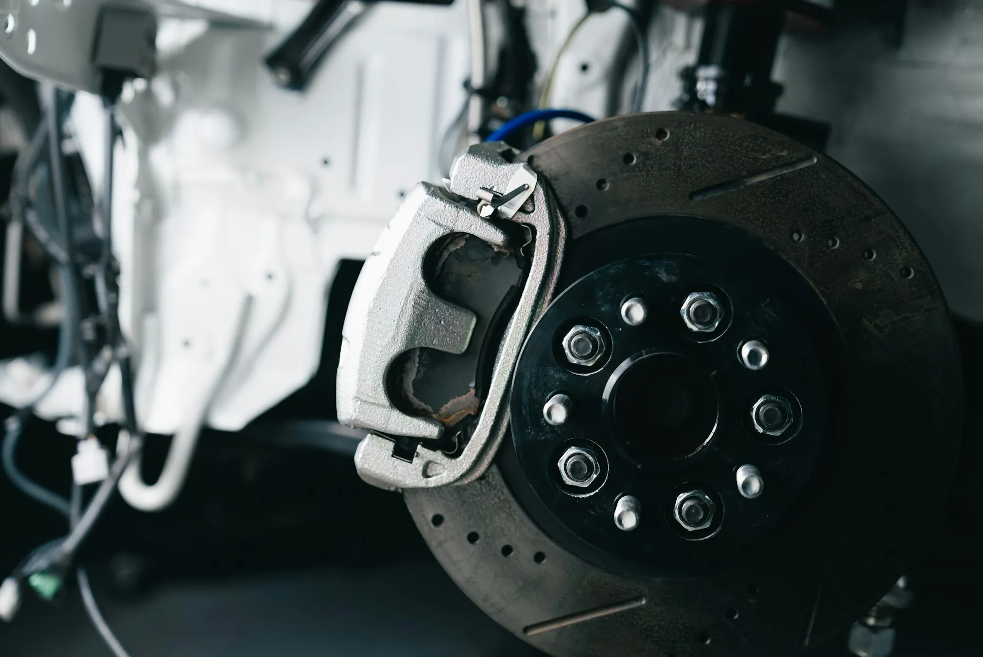 Close view of a drilled brake rotor and caliper on a vehicle in the shop