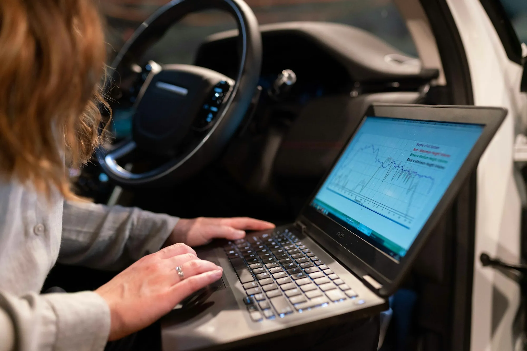 Technician reading diagnostic data on a laptop inside a vehicle