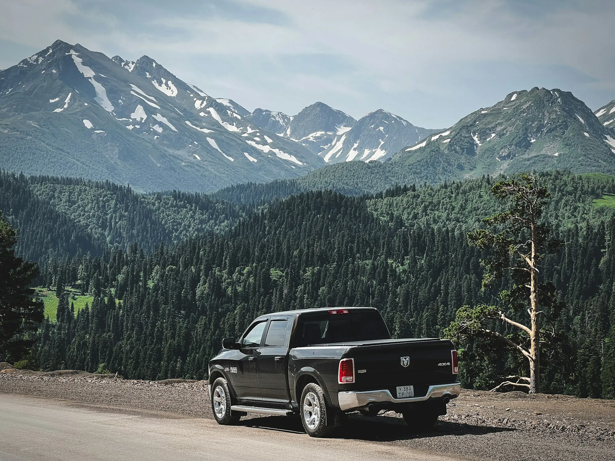 Dark pickup truck parked on a mountain road with snow-capped peaks behind it