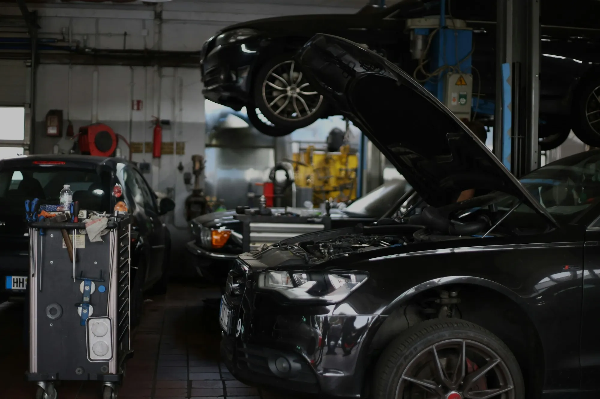 Dark sedan with its hood open inside a repair shop bay