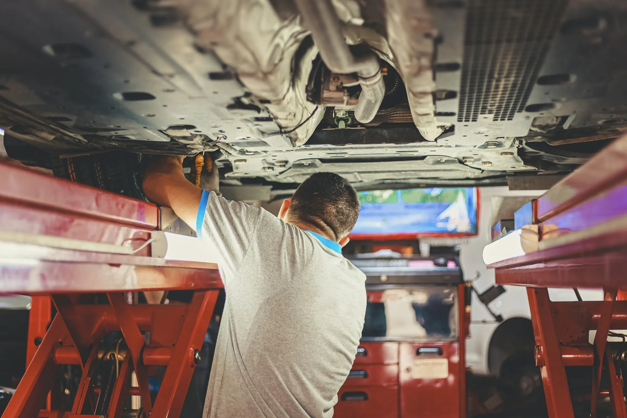 Technician working beneath a vehicle raised on a shop lift